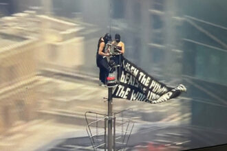 Two people climb to the top of Empire State Building with massive banner